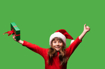 A smiling little girl in a Santa hat shows a beautifully wrapped present. Merry Christmas and Happy New Year 2023. Portrait isolated on green background
