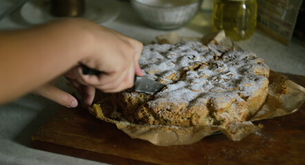 A woman's hand cuts a ready-made Charlotte apple pie into equal parts with a knife in the kitchen on a wooden board