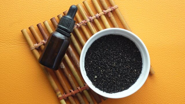 Black Cumin in a container and oil in a jar on table.