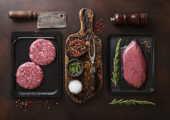 Fresh raw beef fillet steak and mince burgers in vacuum tray with barbeque utensils and spice on...