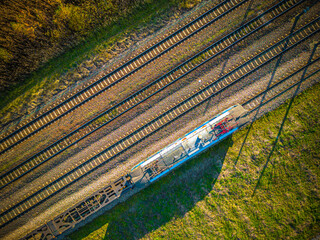 Aerial view of cargo train, a double-track railway in countryside. Railroad with green grass and trees with long shadows, top view. Transport infrastructure, train track, summer nature