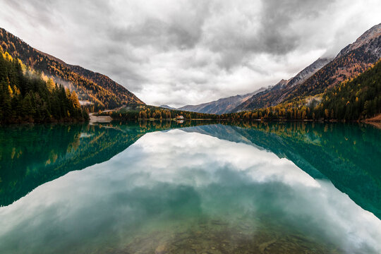 Perfect symmetrical reflection of dramatic clouds and autumn mountains in the crystal clear water of Lake Anterselva, South Tyrol, Italy. Beautiful alpine lake landscape in Puster Valley.