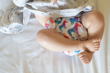 A baby lying on a bed with the focus on the baby's legs. She is wearing a modern, reusable cloth...