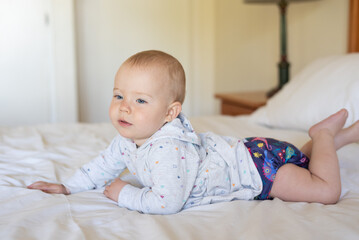 A happy, content baby lying on her stomach doing tummy time to strengthen her back. She is wearing a modern, reusable cloth diaper