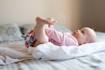 A happy and content baby girl lying on a bed. She is wearing a modern, reusable cloth diaper.