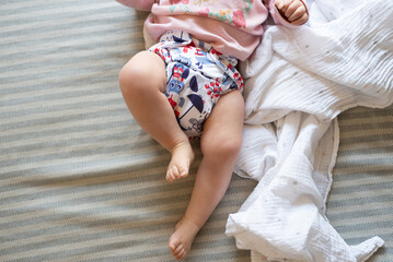 A baby lying on a bed with the focus on the baby's legs. She is wearing a modern, reusable cloth...