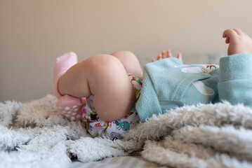 A baby lying on a bed with the focus on the baby's legs. She is wearing a modern, reusable cloth diaper with a pretty print. - obrazy, fototapety, plakaty