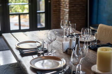 side view of table setting with crockery on wooden table with plates, wine glasses, forks, knives, napkin holders