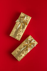 Gift wrapped in gold foil. Christmas present with gold ribbon on red background. Top view.