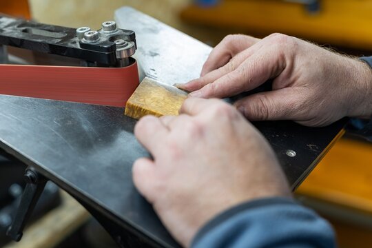 Industrial tool worker grinds a wood handle on a rotating belt sander, he makes a knife handle. - Powered by Adobe