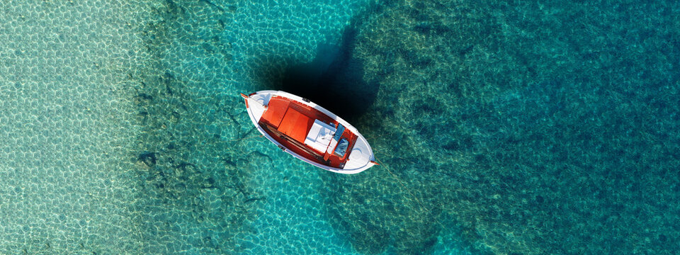 Aerial drone ultra wide panoramic top view photo of red wooden traditional fishing boat in turquoise sea shore of Mykonos island, Cyclades, Greece