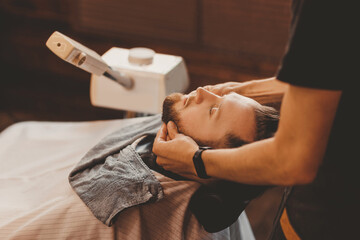 Hairdresser massages man face to improve hair growth and skin care. Preparing and softening beard...