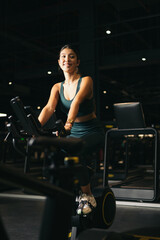 Fototapeta na wymiar Young Asian woman on a bicycle doing spinning in a gym. Young woman exercising on gym bike. cardio concept.