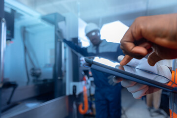 Industry african worker in helmet holding tablet, background engineer use CNC machine blue color. Concept team work industrial workshop