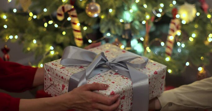 Male hands giving present gift in christmas wrapping paper to female hands. Person holding box tied. Concept of family holidays, perfect Christmas, New Year.