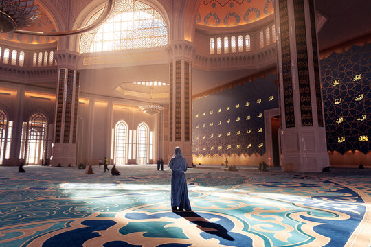 Back view modern woman in traditional blue abaya standing in Grand Mosque with magic sun light. Concept traveling islam arab culture