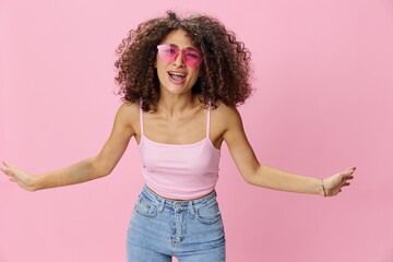 Woman with curly afro hair with sunglasses model poses on a pink background in a pink T-shirt, free movement and dance, look into the camera, smile with teeth and happiness, copy space