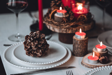 Rustic table decor for Christmas or New Year family dinner. Centrepiece with red candle, dry orange, cone, cinnamon, anise. Zero waste eco-friendly home. Cozy atmosphere, dark background. Close up