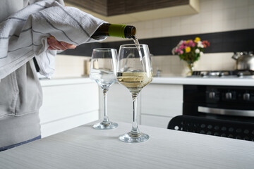 Woman pours white wine into glasses. Two glasses of white wine on the kitchen table. Celebrate and enjoy the moment. Tasting of alcoholic beverages. Glass of wine close-up