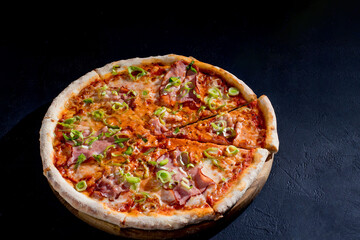Delicious pizza with mozzarella cheese, ham, leeks on a tomato base on black background