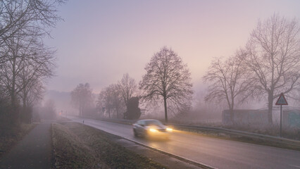 car with headlights on driving through the fog in the morning
