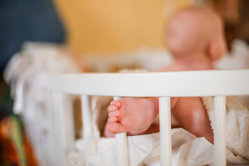 Small legs of a newborn baby. Baby in diaper lying in a comfortable safe crib in the bedchamber
