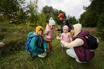 Mother and children searching mushrooms in the wild forest.