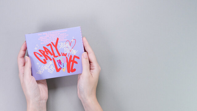 Hands holding Itzy CRAZY IN LOVE 1st Album on grey background. Special edition music CD. South Korean girl group Itzy. Space for text. Gatineau, QC Canada - November 10 2022
