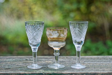 a row of white brown three glass crystal goblets on a gray wooden table outdoors on a green background