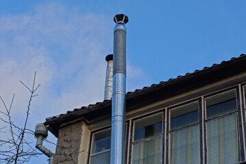 one gray long metal pipe chimney on a brown loft and windows against the blue sky