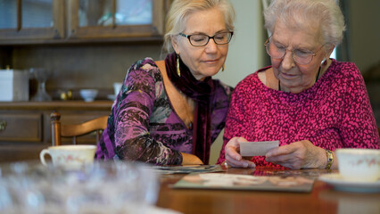 Extreme closeup of senior elderly smiling woman looking at old photos and remembering memories with daughter at the dining room table.