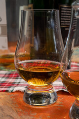 Tulip-shaped tasting glass with dram of Scotch single malt or blended whisky on wooden table with tartan