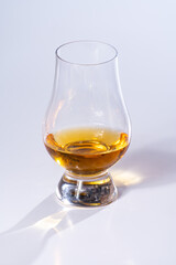 Tulip-shaped tasting glass with dram of Scotch single malt or blended whisky on white background