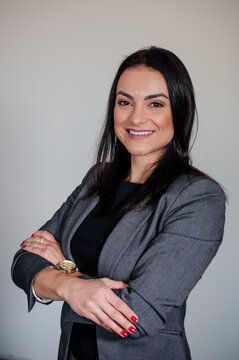 A mulher empreendedora em uma sess&atilde;o de fotos corporativa em pose de p&eacute; sorridente vestida elegantemente com palet&oacute; e com bra&ccedil;os cruzados