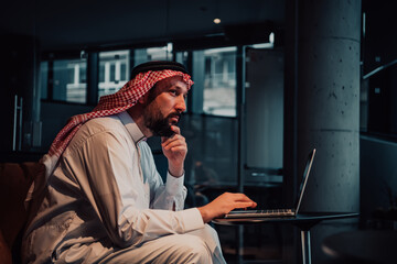 An elderly Arab man sitting in the office and analyzes data on his laptop