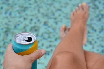Woman holding aluminum can with beverage near swimming pool, closeup