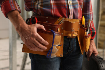 Professional builder with tool belt indoors, closeup