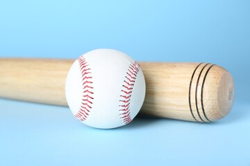 Wooden baseball bat and ball on light blue background, closeup. Sports equipment