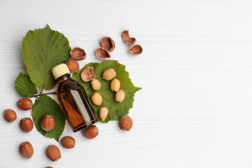Bottle of hazelnut essential oil and nuts on white wooden table, flat lay. Space for text
