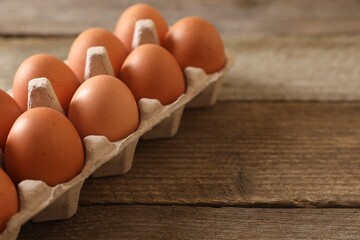 Raw chicken eggs in carton on wooden table, closeup. Space for text