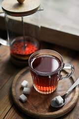 Glass cup with delicious tea and sugar on wooden table, closeup