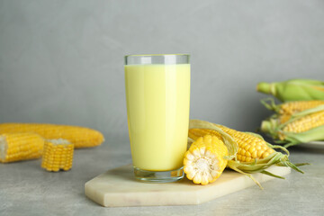 Tasty fresh corn milk in glass and cobs on light grey table