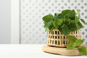 Fresh lemon balm in wicker basket on white table, space for text