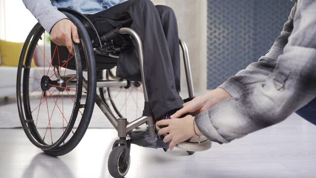 Girlfriend helping her paraplegic boyfriend. Care and disability concept.
Woman helps paralyzed legs of a disabled person sitting in a wheelchair.
