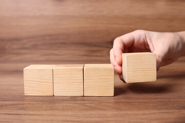 Woman arranging cubes on wooden background, closeup with space for text. Idea concept