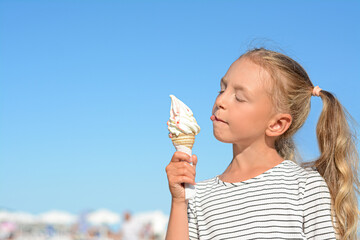 Adorable little girl with delicious ice cream against blue sky, space for text