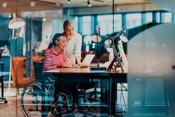 Businesswoman in a wheelchair working in a creative office. Business team in modern coworking office space. Colleagues working in the background at late night.