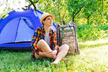 Naklejka na ściany i meble Defocus young woman sitting near camping tent outdoors surrounded by beautiful nature. Freelance, sabbatical, mental health. Rest. Summer camp. Dream. Out of focus