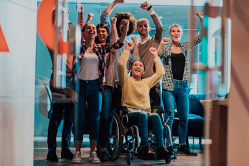 Photo of business women in wheelchairs with their hands raised in the air with their colleagues,...