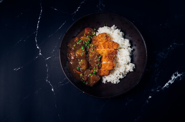 Japanese chicken katsu curry rice, deep fried breast chicken fillet with beef, carrot and potato curry in black plate on wooden table Crispy fried pork cutlet with curry rice  - Japanese food style